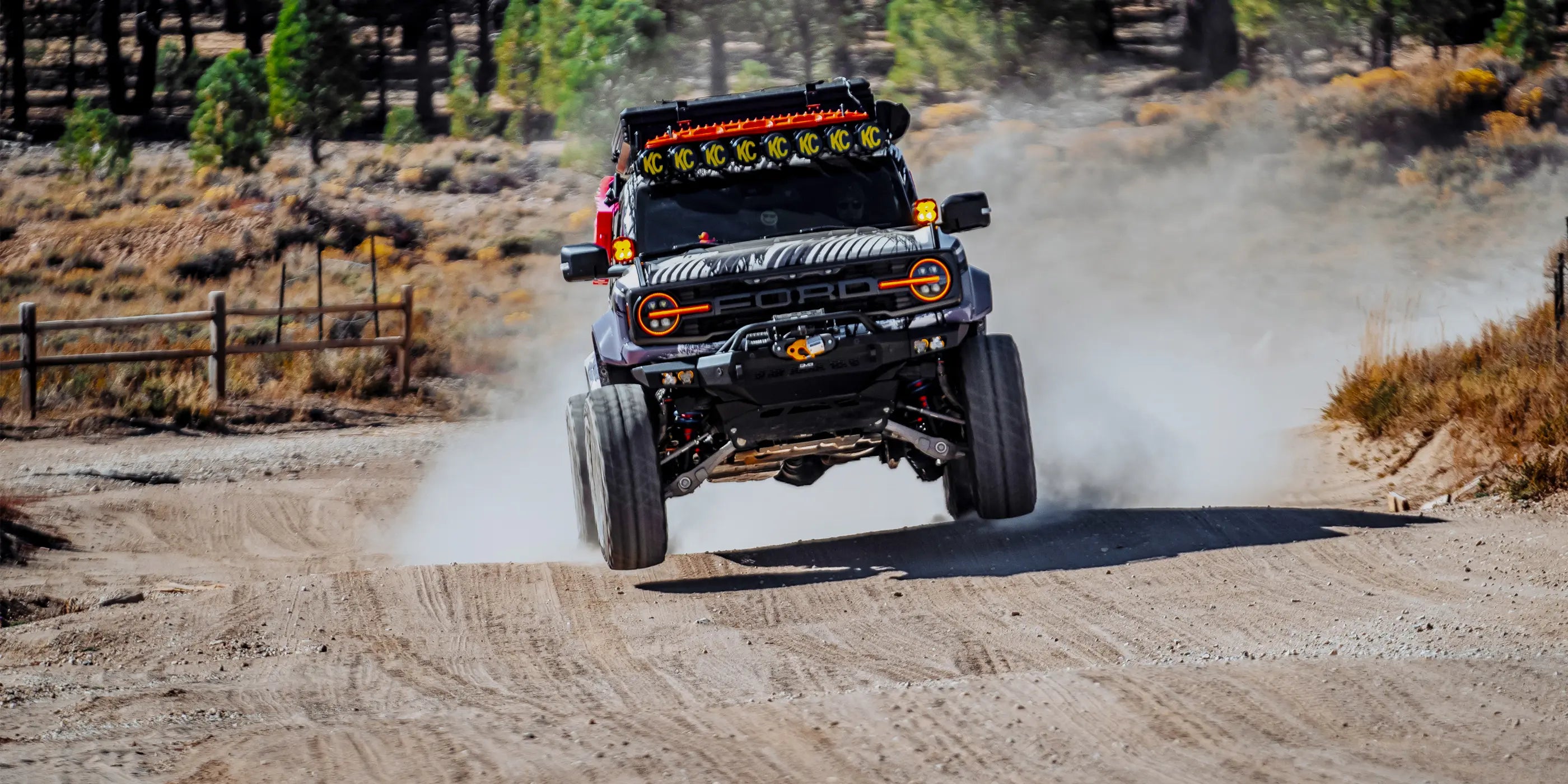 Ford Bronco driving on a dirt road with trees and open space in the background