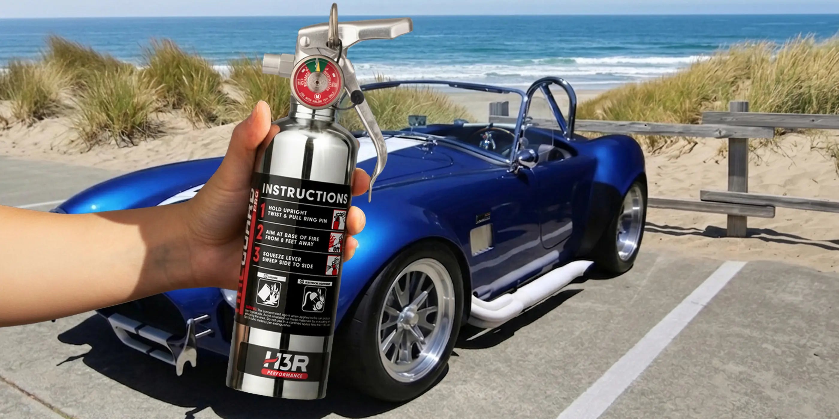 Blue Shelby Cobra parked at a beach overlook with a hand holding an H3R Performance HalGuard PRO fire extinguisher in the foreground.